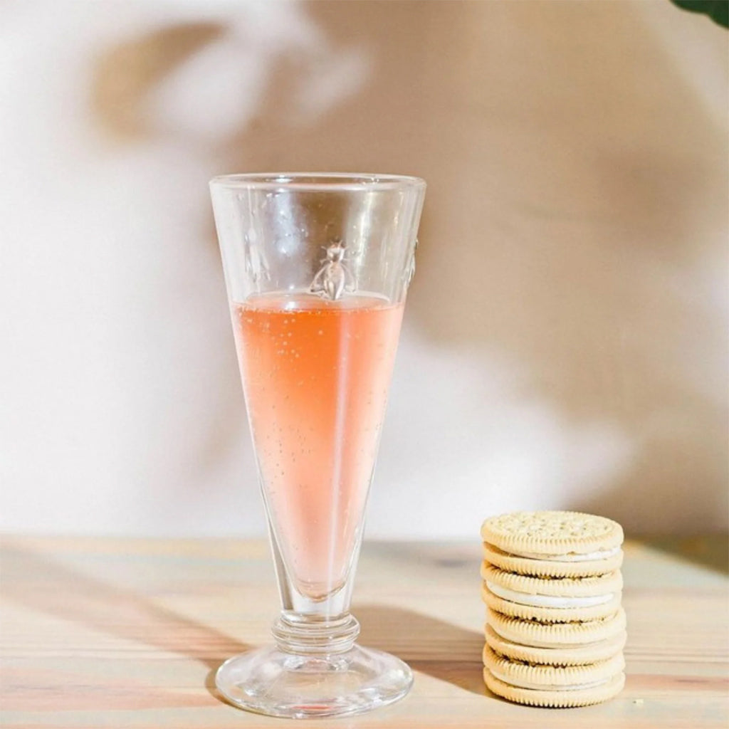 La Rochere Bee Champagne Flute positioned next to a stack of cookies, arranged on a wooden table.